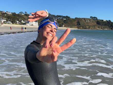 Nageuse en combinaison sortant de l'eau sur une plage, signe de victoire