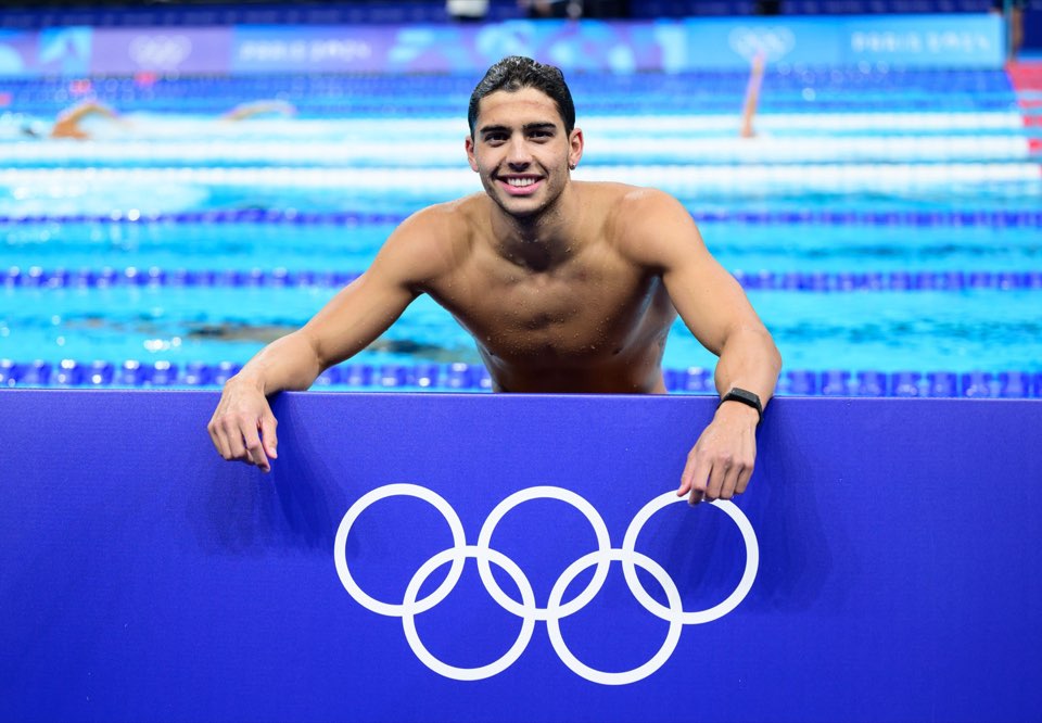 Amazigh Yebba accoudé à la balustrade devant les anneaux olympiques
